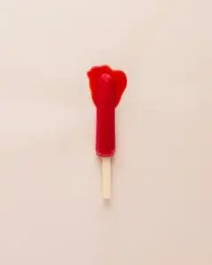 Photo artistique représentant une glace à l’eau rouge fondue sur un fond rose pâle, évoquant de manière subtile et métaphorique le thème des menstruations.